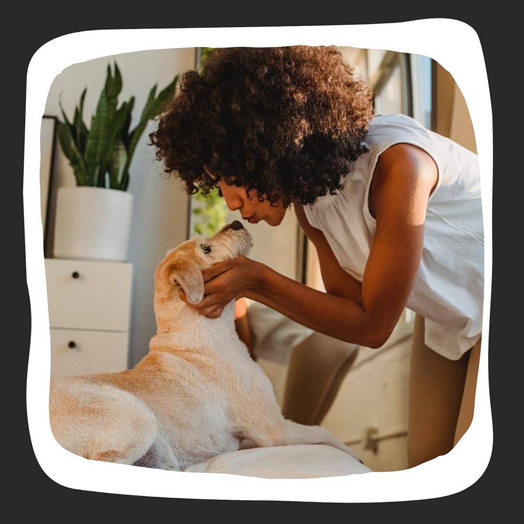 Black woman with tan dog making a kissing face to the dog